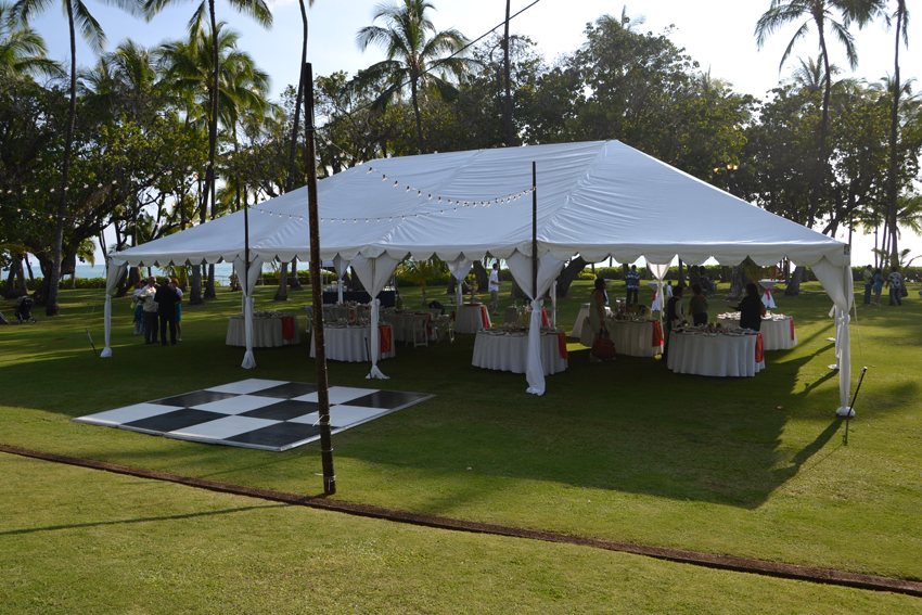 A white frame tent with a black and white dance floor on a lawn by the beach
